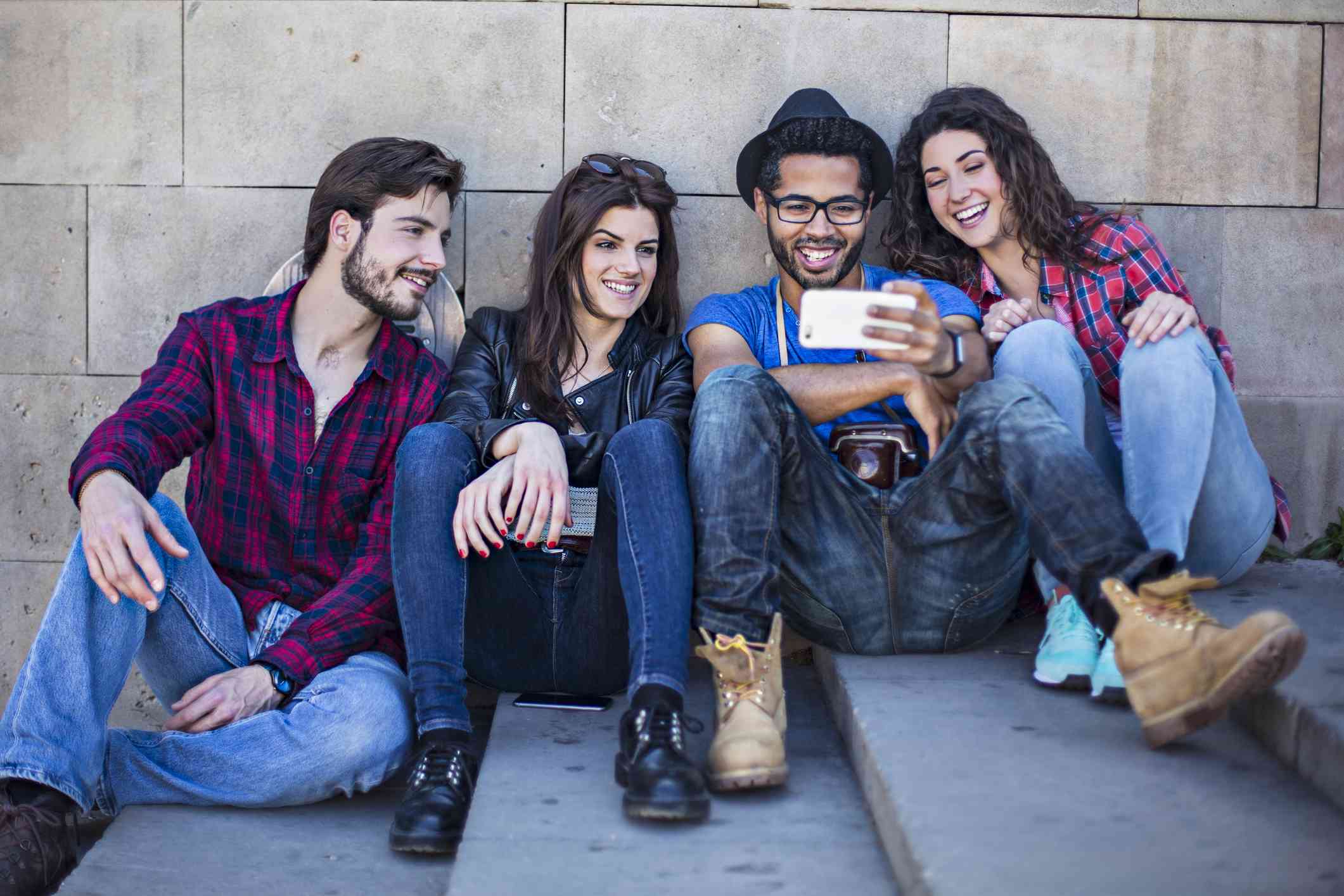 Четверо друзів дивляться фільм на смартфоні, сидячи на відкритому повітрі на бетонних сходах.