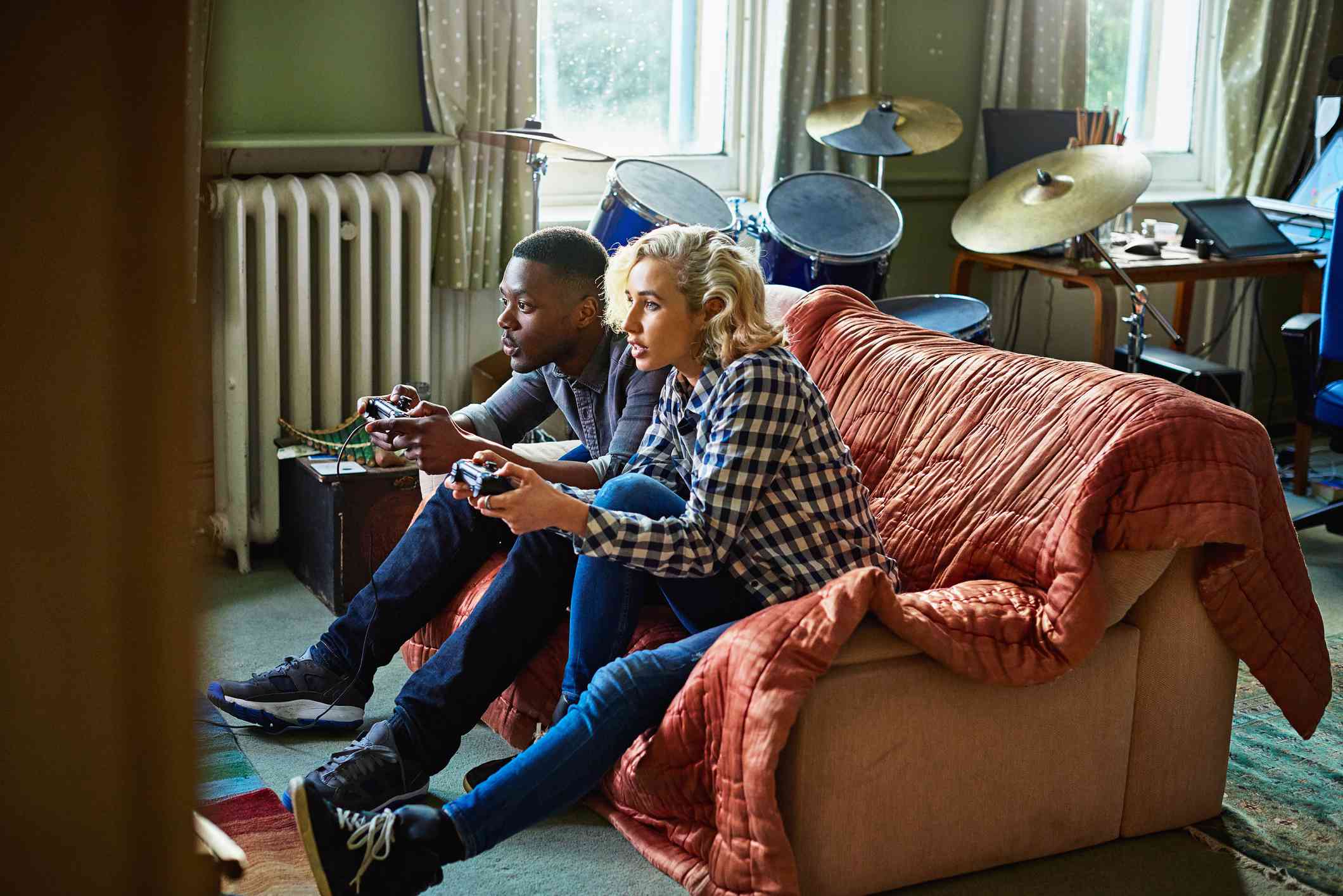 Двоє молодих людей, що грають у консольні відеоігри, сидячи на дивані в невеликій квартирі.