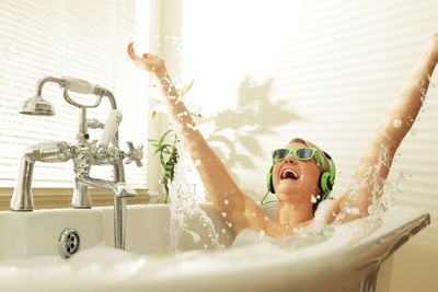 Жінка в зелених сонцезахисних окулярах та навушниках хлюпалися у ванній
