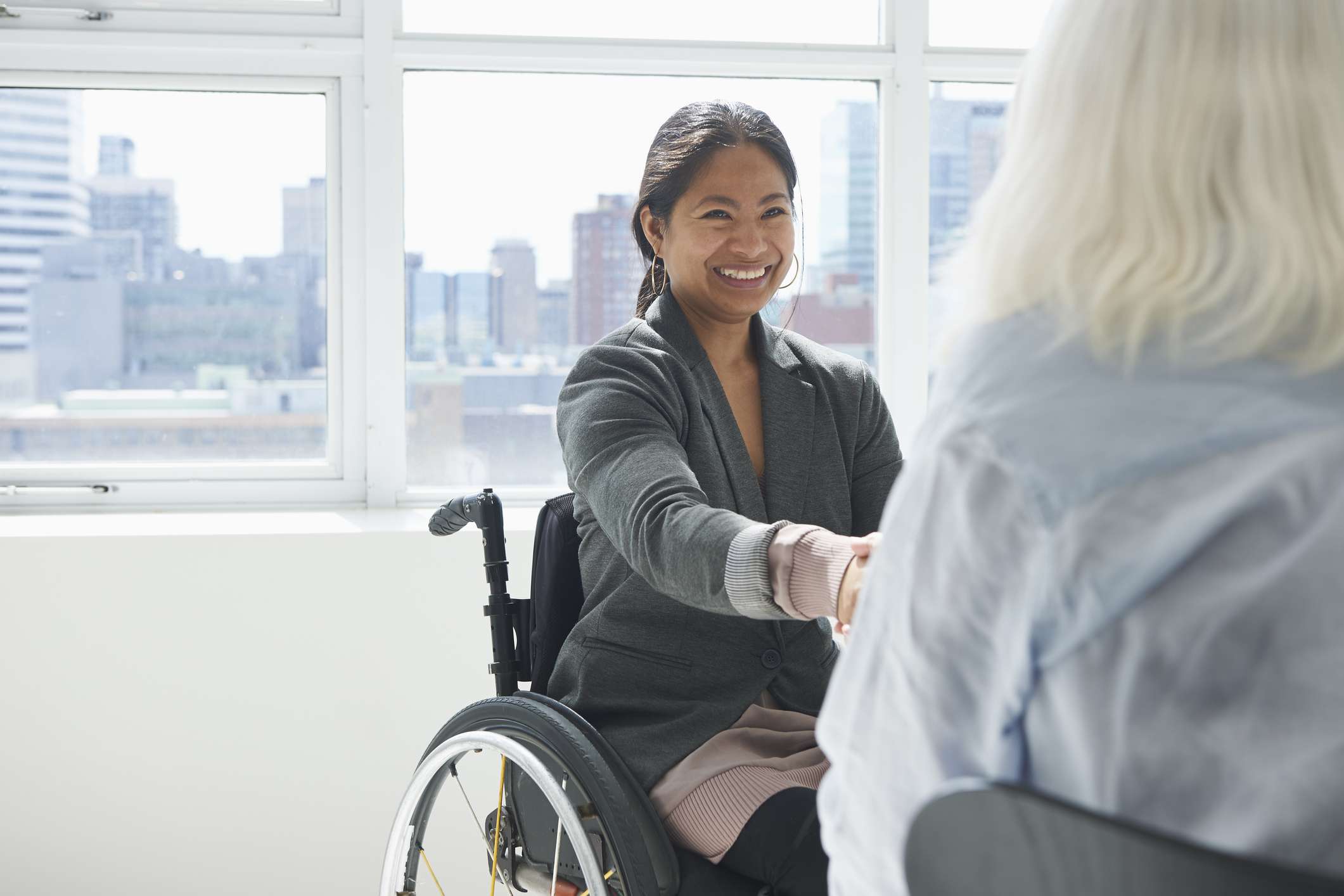 Бізнес-леді в інвалідному візку, потискує руку іншій людині