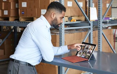 Чоловік у костюмі торкається свого Microsoft Surface Pro 7 під час відеоконференцій з друзями та колегами.