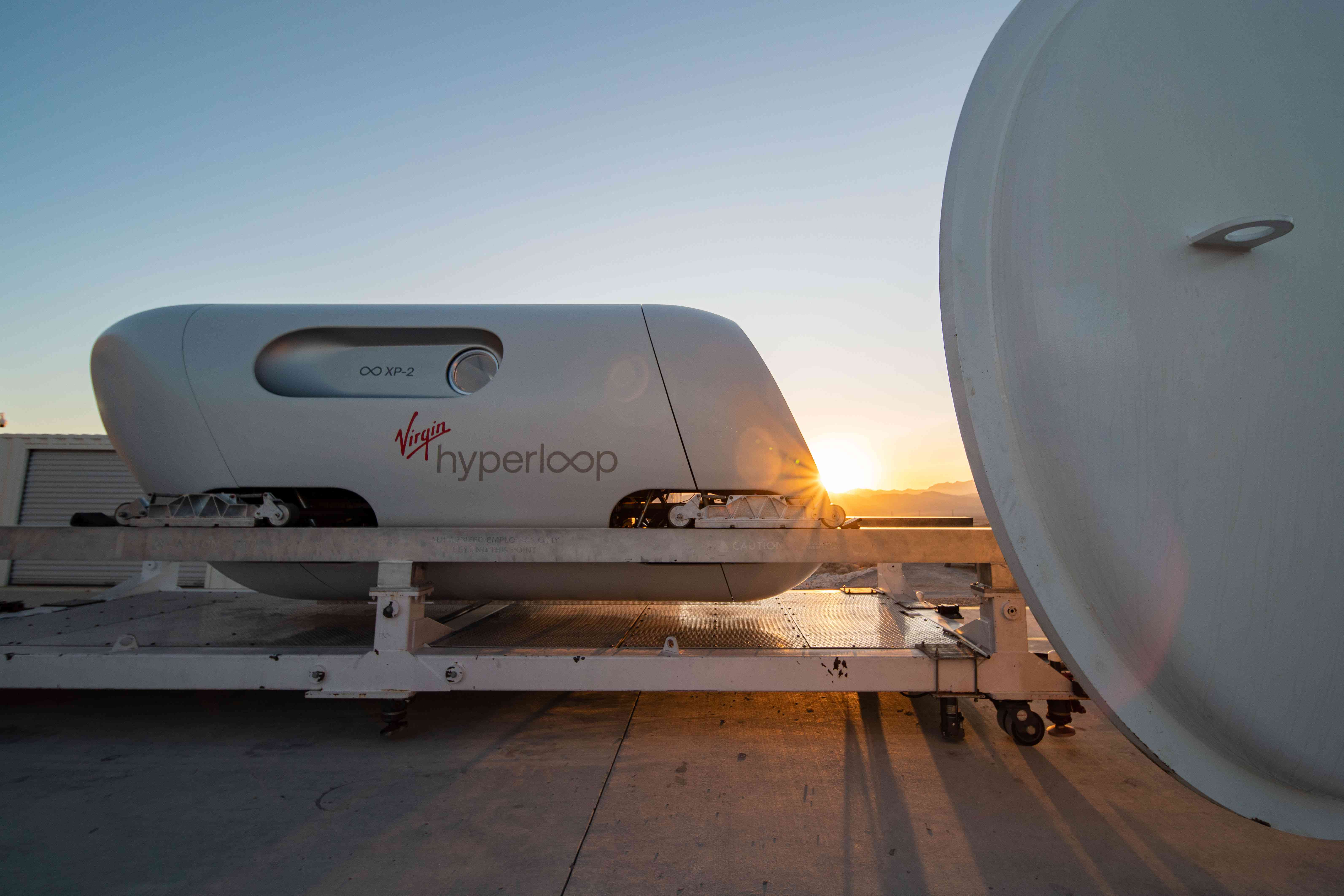 Тестовий стручок Virgin Hyperloop, що лежить на платформі із заходом сонця за ним