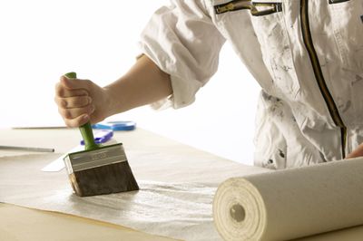Person uses a large brush to apply paste to a roll of paper.