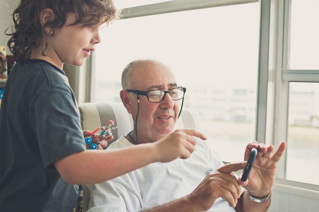 Бабуся, дідусь та онук взаємодіють зі смартфоном, а дитина тримає крихітного робота.
