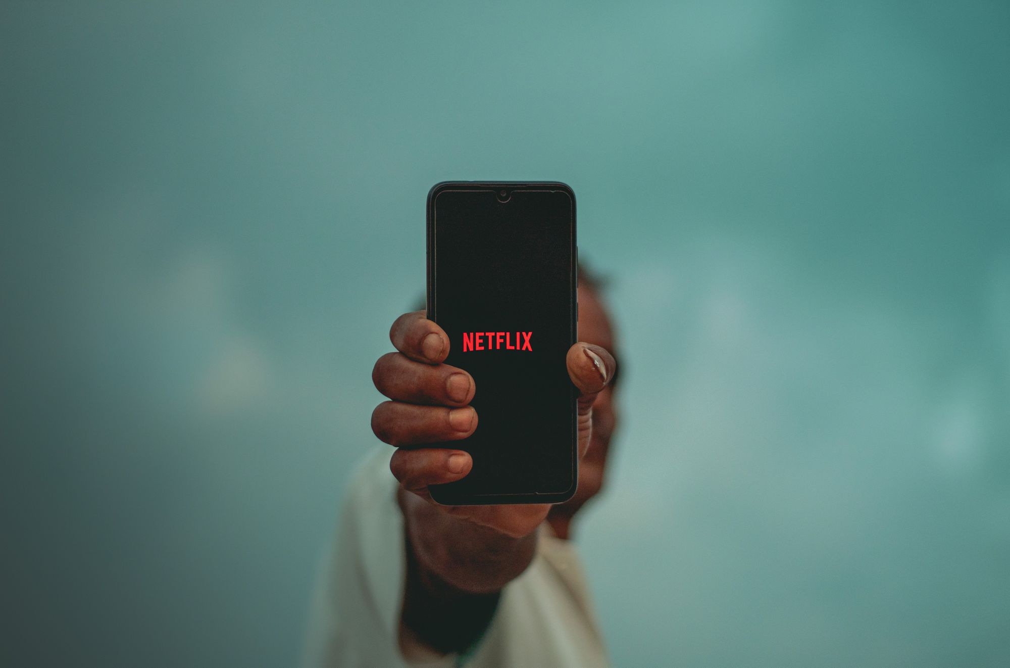 Людина тримає чорний iPhone на відстані витягнутої руки з логотипом Netflix на екрані. 